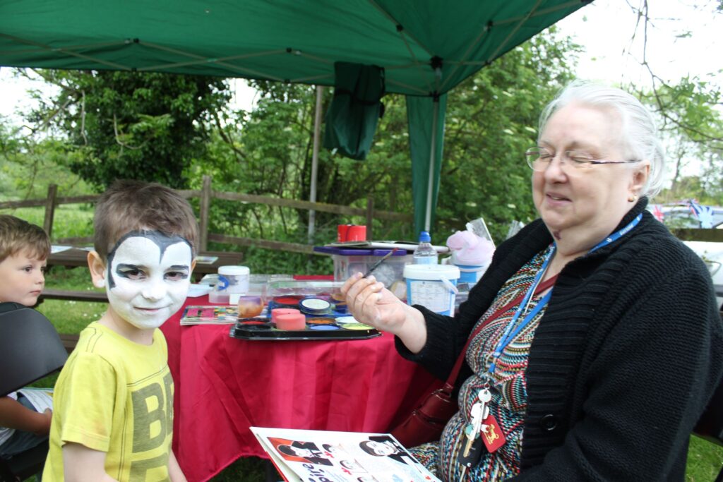 An older woman face painting a child in a pub garden