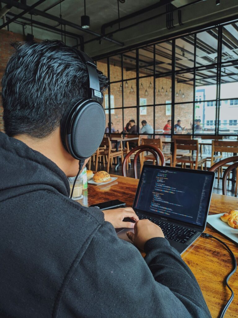 Picture of a man with headphones working at his laptop in a busy bar.