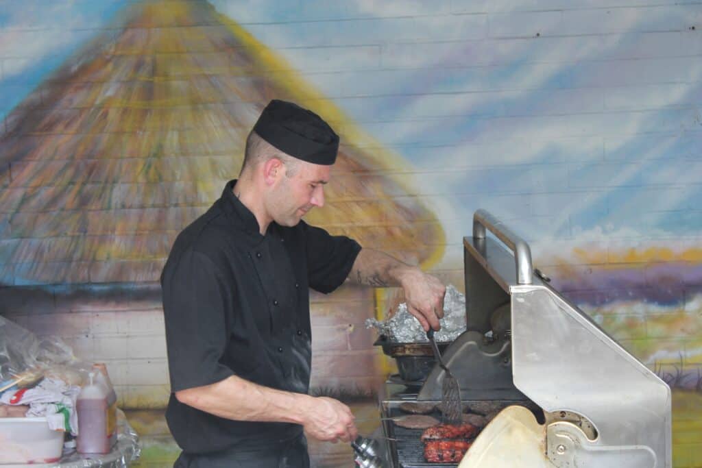 A chef dressed in black with a black hat cooking at a BBQ