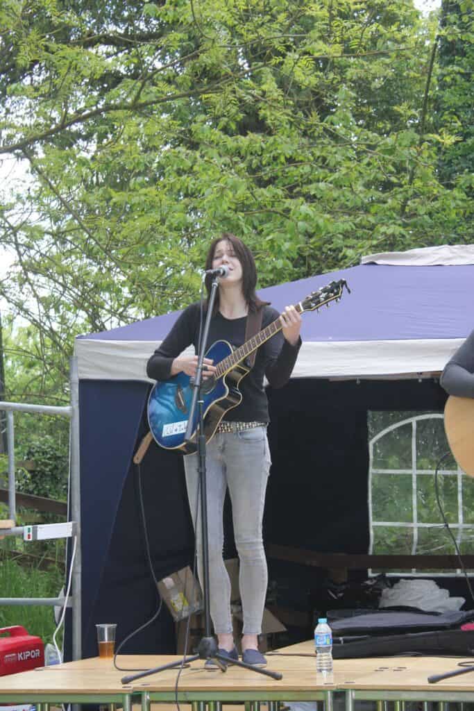 A woman playing the guitar and singing in a pub garden, showing the link between events and encouraging locals to use your pub.